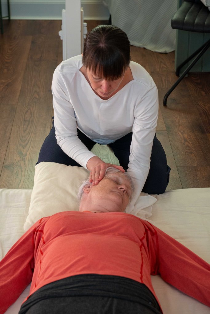 Liz kneeling behind the receiving whilst applying  Shiatsu touch to their face